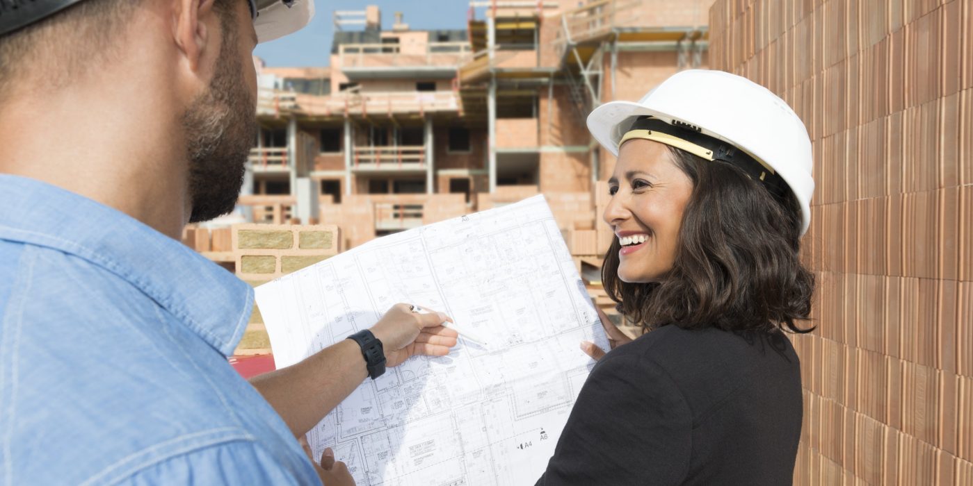Male and female Architect with technical drawing on construction site