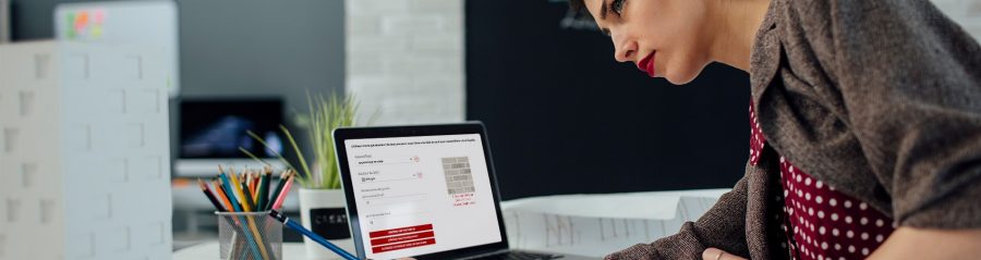 Female architect working in her new modern office. Standing and examining blueprints for her new project. There are on the desk in front of her laptop, architectural model on new business building and color swatch.